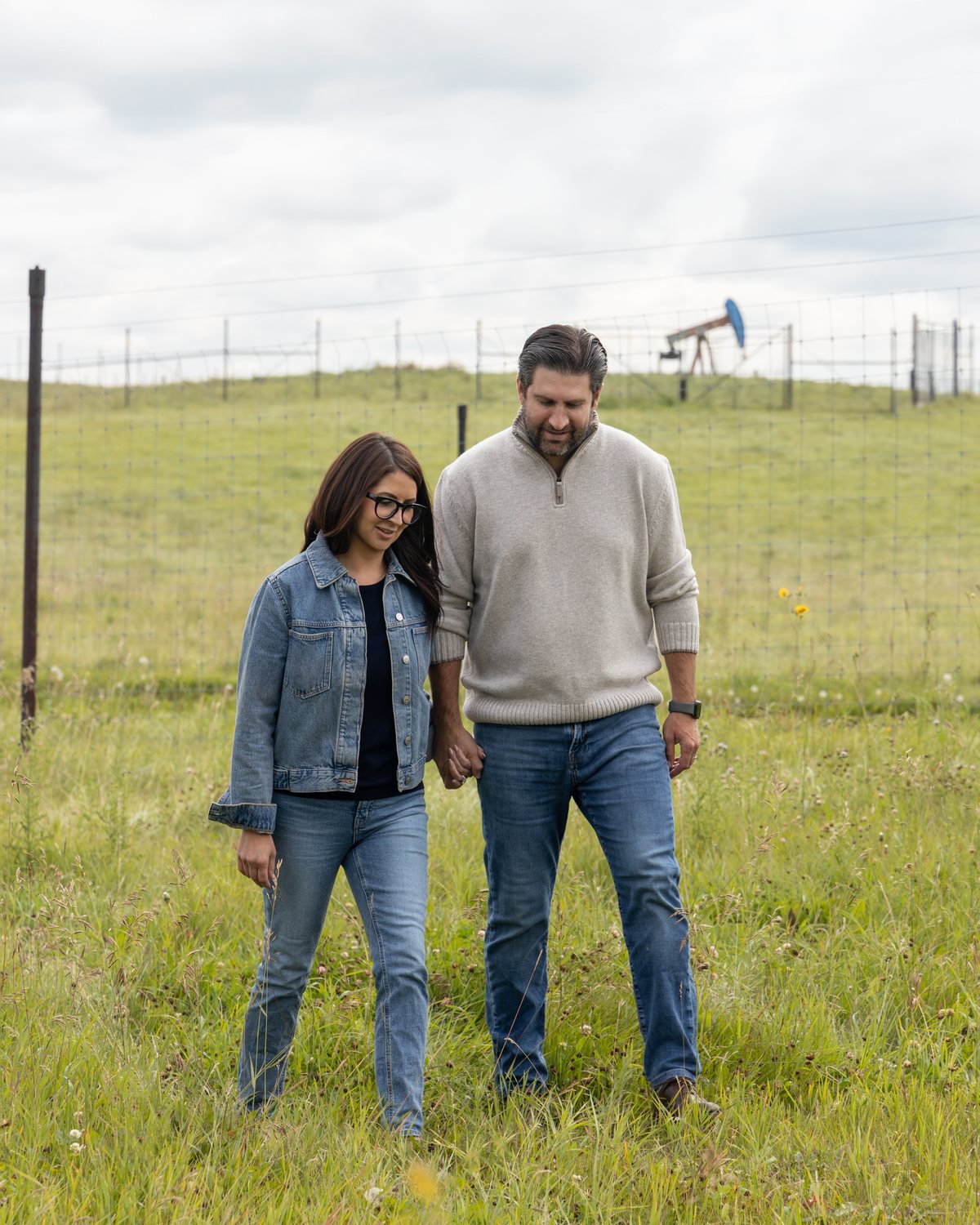 Ben Lotery and his wife walking a field in the riding, a pumpjack on the rise behind them