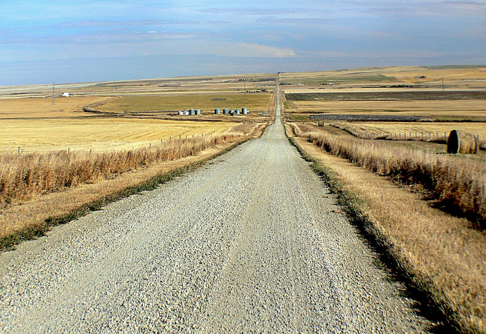 A gravel road running straight through harvested fields under a wide Alberta sky