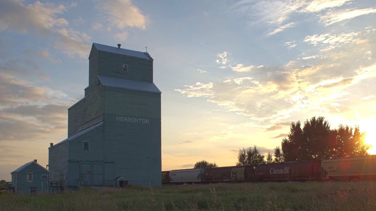 A prairie grain elevator lit by low golden sun beside the rail line