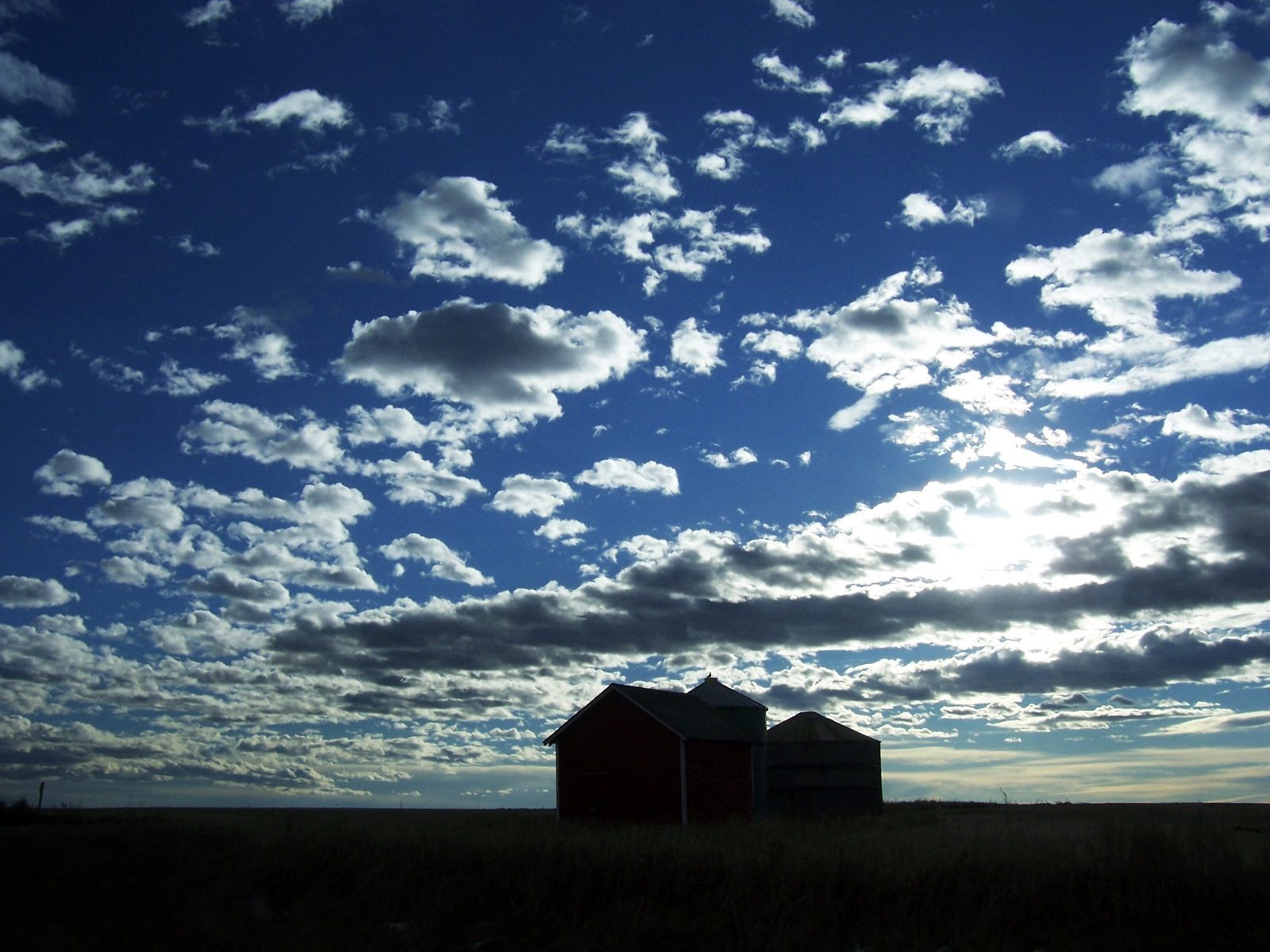 An isolated barn silhouetted against a dark, broken sky at dusk on the Alberta prairie